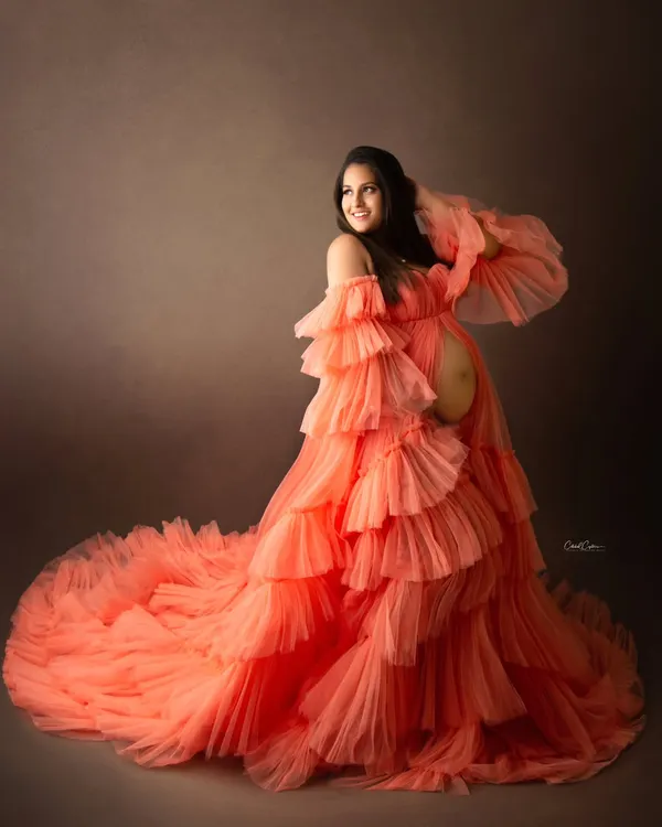 A truly showstopping maternity portrait. This mom-to-be looks radiant in a magnificent, multi-layered orange tulle gown that creates incredible texture and volume.