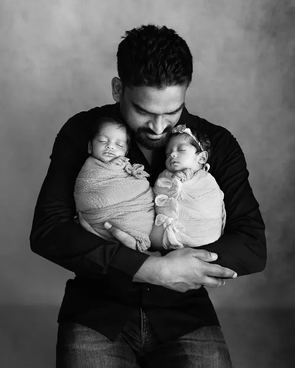 A new father holds his twin newborn babies, one in each arm. This powerful black and white portrait captures the overwhelming love and pride of a dad on Father's Day.