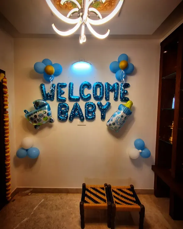 A simple 'Welcome Baby' decoration for a home. This includes a blue foil balloon banner and other small balloon accents like a bottle and an airplane.