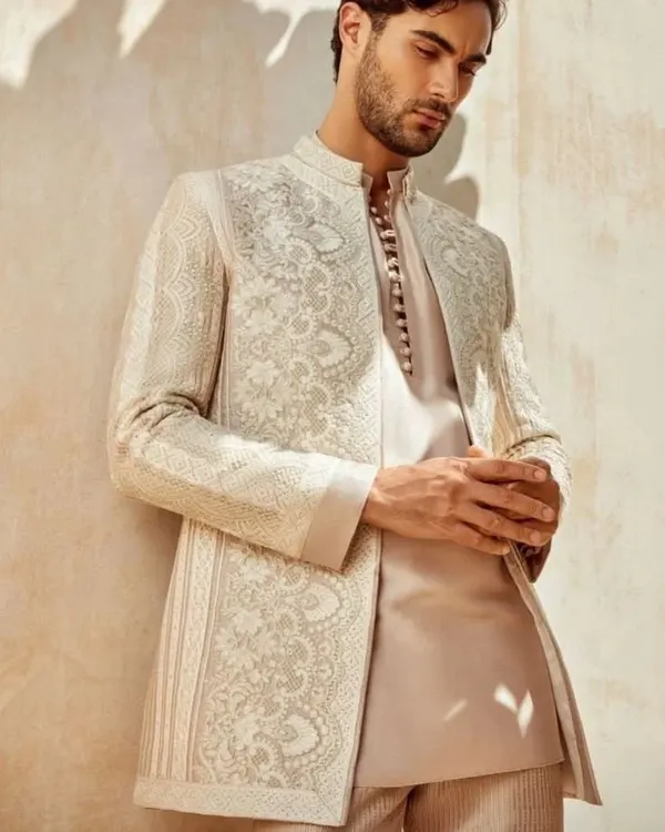 A model showcases a sophisticated off-white sherwani jacket with intricate self-colored embroidery. This piece is a perfect example of understated elegance, ideal for the modern groom who appreciates fine craftsmanship.
