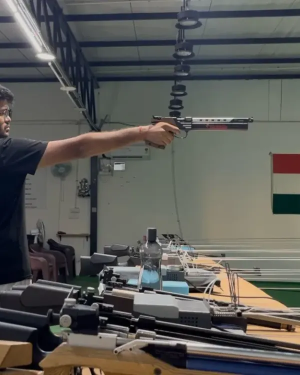 A shooter demonstrates a perfect one-handed stance during air pistol training, with the Indian flag symbolizing the ultimate goal.