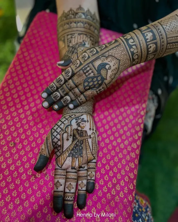 A truly personal bridal mehendi featuring a portrait of the groom on one hand and a peacock on the other. The arms are adorned with elephant motifs and jharokha patterns, creating a royal narrative.