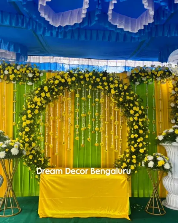 A classic Haldi decor with a vibrant yellow and green backdrop. The floral arch made of yellow chrysanthemums and hanging marigold strings creates the perfect festive mood.