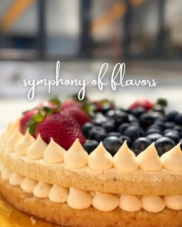 A symphony of flavors, this cake features two layers of light sponge with a creamy filling, piped details, and a generous topping of fresh strawberries and blueberries. It's a celebration of fresh, natural sweetness.