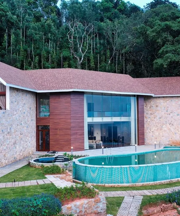 This is our vision for a home that lives in harmony with its landscape. The exterior of this Chikmagalur residence uses natural stone and expansive glass to merge with the mountain scenery, creating a sanctuary that is both grand and grounded.