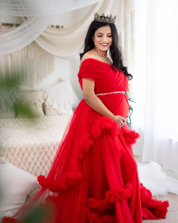 A vision in red. This mom-to-be radiates joy in one of our ruffled tulle gowns, complemented by a delicate crown and our bright, airy studio backdrop.