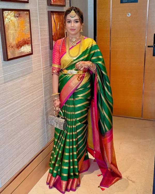A full-length portrait showcasing a complete South Indian look, featuring a vibrant Kanjivaram saree and layered temple jewellery.