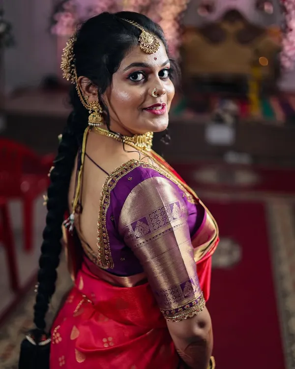 A classic bridal portrait showing the intricate details of the blouse, gold jewelry, and traditional braided hairstyle. This over-the-shoulder pose is timeless and elegant.