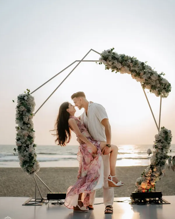 A beautiful moment from a Goa beach proposal shoot. I can help you plan and capture this once in a lifetime event, complete with romantic setups like this floral arch against the sunset.