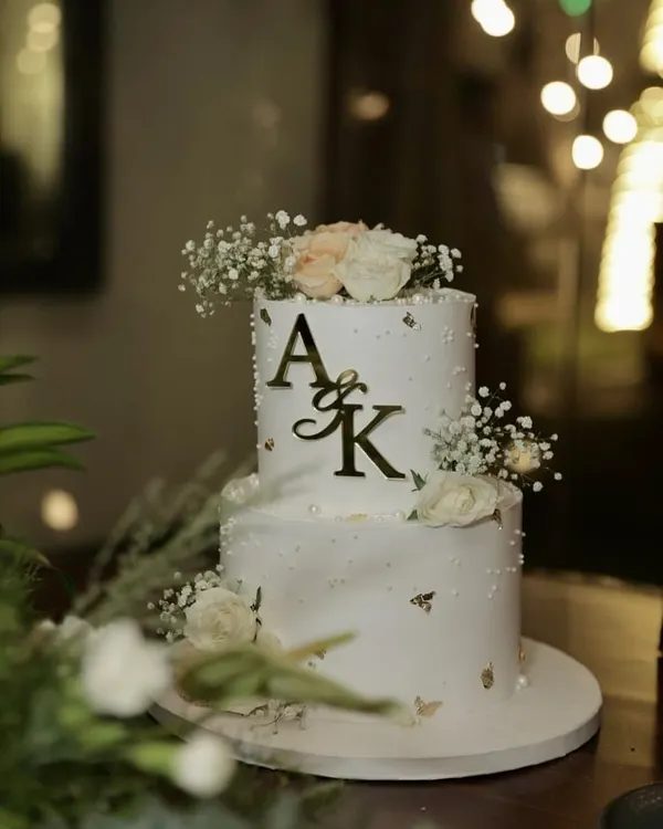 This two-tiered engagement cake captures the mood of a forever story beginning. Set against romantic lighting, the design features a custom gold monogram, delicate baby's breath, and flecks of gold leaf for that touch of luxe. ✨