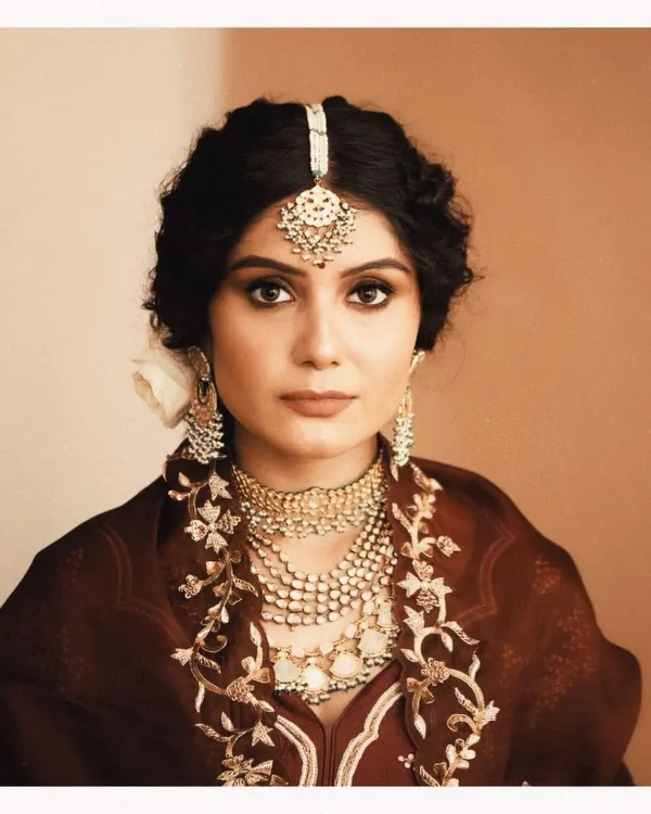 A classic bridal portrait that captures a moment of quiet reflection. We styled this look with heavily layered polki and pearl necklaces, a traditional maang tikka, and a rich maroon outfit to create a vintage, almost Mughal-inspired aesthetic.