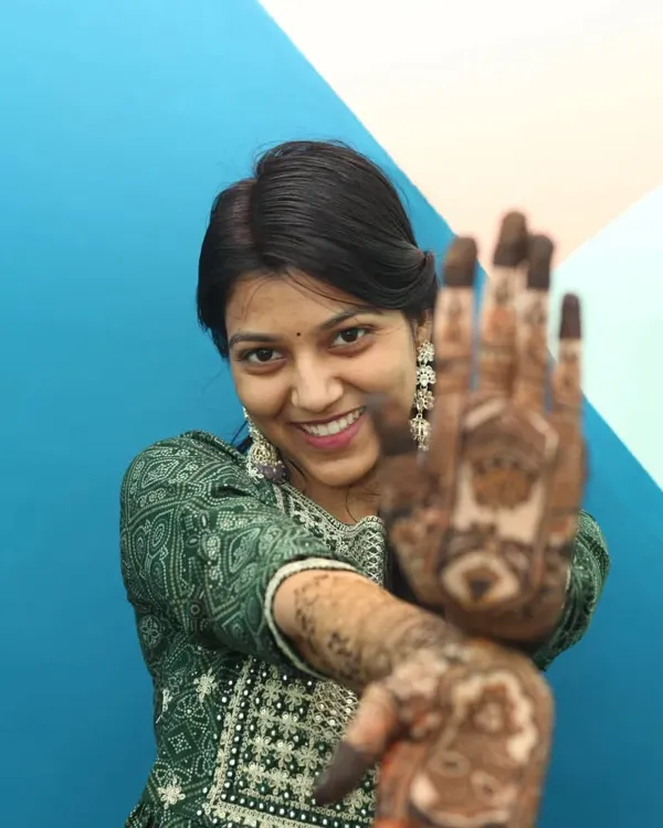 A classic portrait from a Mehandi photoshoot. The focus here is on the beautiful henna art, with the subject smiling brightly as she shows her decorated hand to the camera.