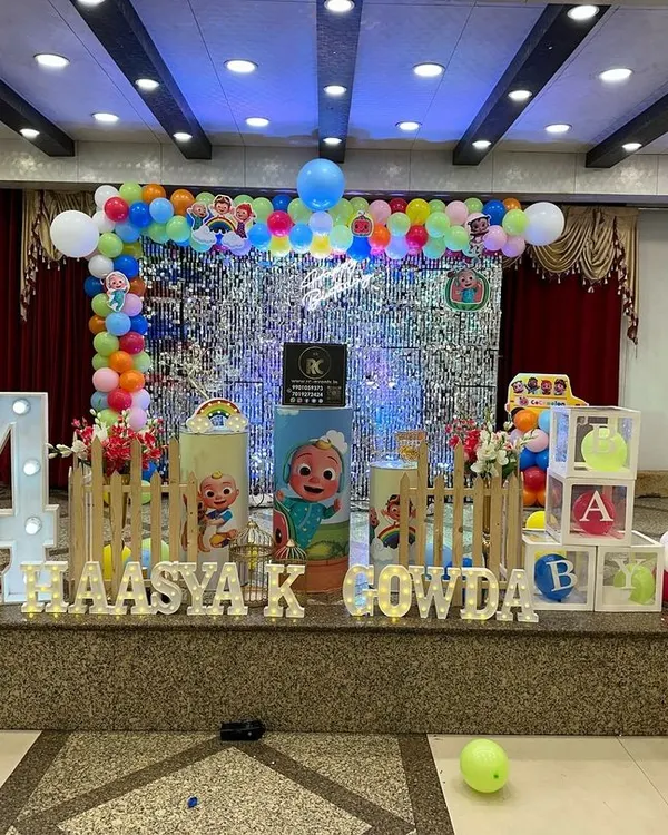 A fantastic Cocomelon stage for a fourth birthday. This setup features a silver shimmer wall, a rainbow balloon arch, character cutouts, and a large marquee number '4'.