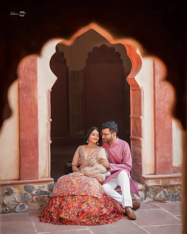 Framed by a traditional archway, this quiet moment captures the regal elegance of a palace romance. The couple's coordinated ethnic wear complements the heritage architecture perfectly.