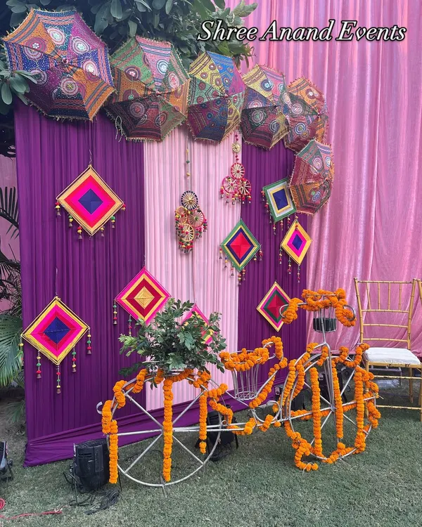 A quirky and colorful Mehndi corner, featuring a bicycle adorned with marigolds and a backdrop of Rajasthani umbrellas and hangings.