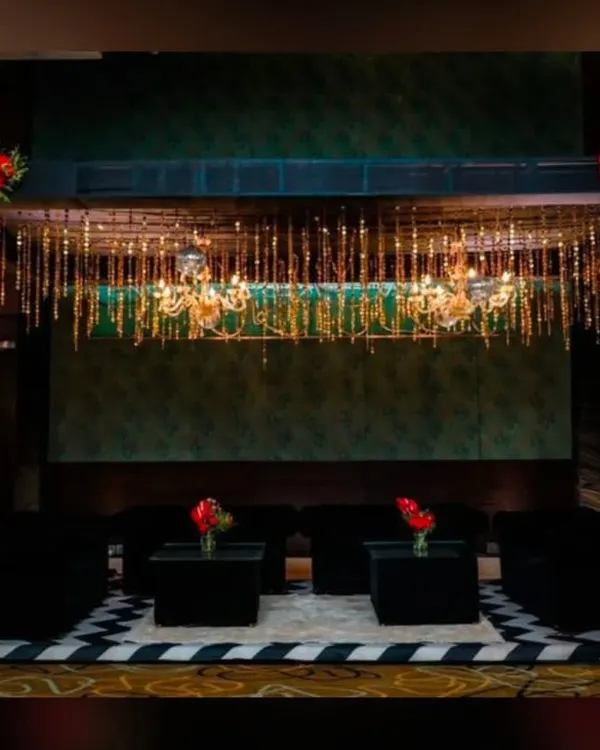 A chic lounge area we created for a corporate event, featuring modern black furniture and a stunning overhead installation of chandeliers and hanging golden tassels. This setup provides a comfortable and stylish space for guests to connect.