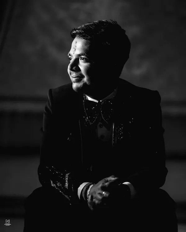 A dramatic black and white groom portrait. Using strong shadows and light (chiaroscuro), this image creates a moody and sophisticated look, highlighting the groom's features in a very cinematic style.