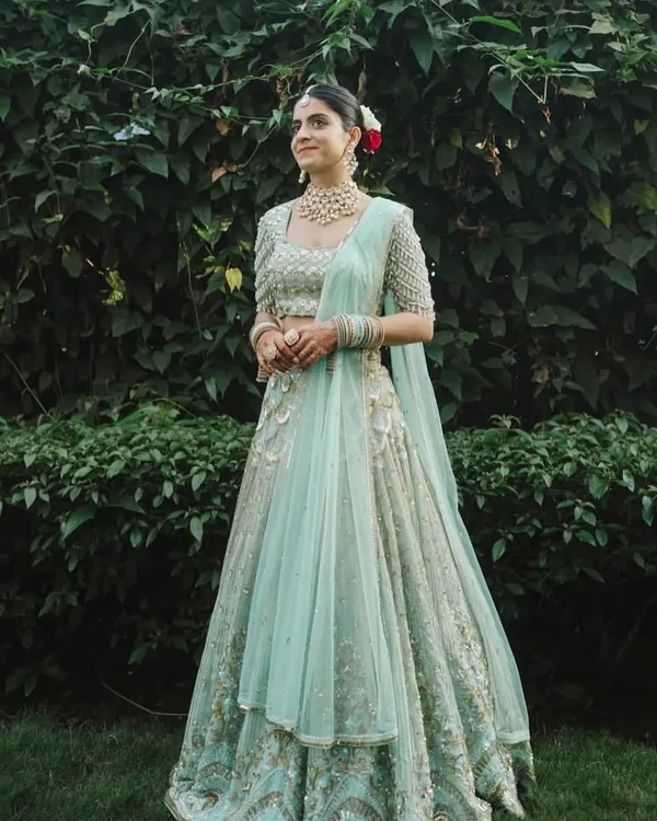 A vision in pastel. Our bride radiates pure joy, adorned in a magnificent uncut polki diamond and pearl choker set that perfectly complements her serene mint green lehenga for her daytime wedding ceremony.