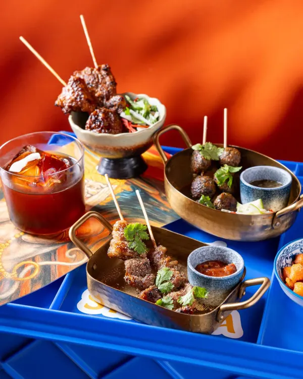 A selection of Asian-inspired appetizers for Banng, served in traditional brass bowls against a bold blue and orange background.