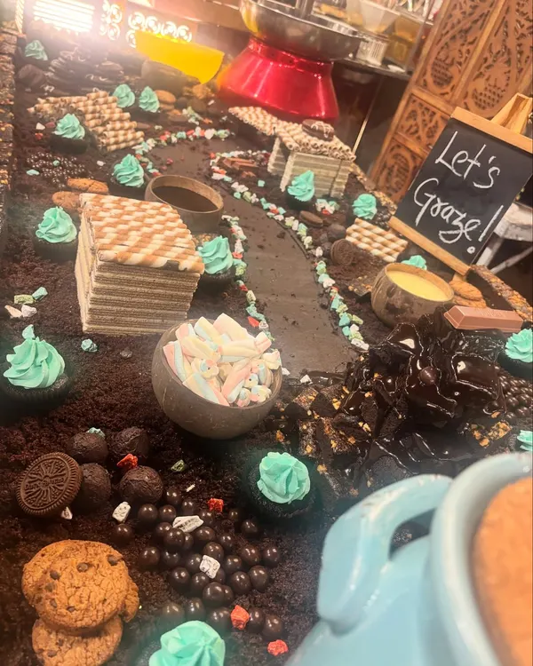 This is my signature chocolate grazing table, designed to be a complete interactive landscape. It features edible chocolate soil, wafer houses, chocolate truffles, cookies, and bowls of marshmallows, all ready for guests to explore and enjoy.