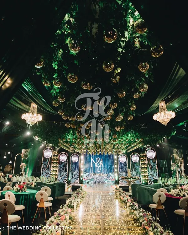 This is our 'Savannah Splendour' Sangeet, where we transformed a ballroom into a tropical wonderland. The design features a lush green ceiling with a cascade of gold mirror balls, a custom glass aisle filled with fairy lights, and opulent seating in jewel tones, demonstrating our capability for large-scale, thematic event production.