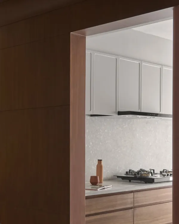 A glimpse into the kitchen, framed by a terracotta lime-washed wall. The design features light grey cabinets and a terrazzo backsplash, blending earthy charm with modern functionality.