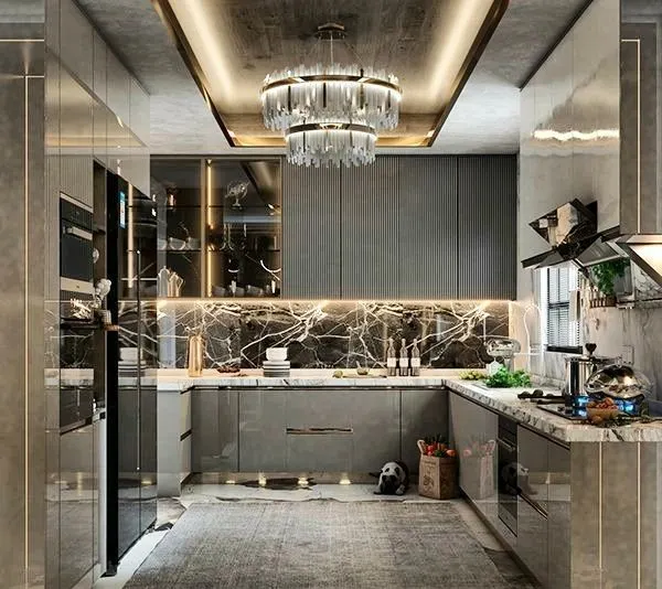 A modern luxury kitchen that balances sleek grey cabinetry and a marble backsplash with a statement crystal chandelier. We love designs that mix functionality with glamour, using elements like coffered ceilings and integrated lighting to elevate the space.