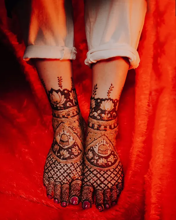 An artistic shot of the bride's feet, adorned with stunningly detailed mehndi designs against a vibrant red background.