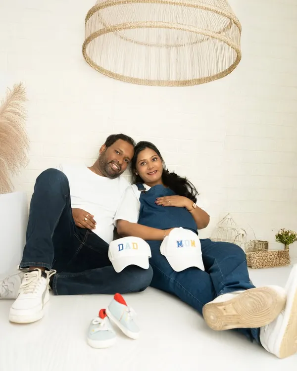A relaxed, casual portrait of a couple in coordinating denim and white. Props like baby shoes and 'Mom' and 'Dad' caps make the shoot personal and fun.