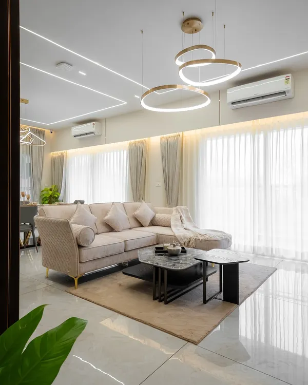 Natural light floods this living room, highlighting the clean lines of the ceiling and the elegant circular chandeliers. The neutral-toned sectional sofa and layered rugs create a calm, inviting atmosphere perfect for relaxation and quiet conversations.