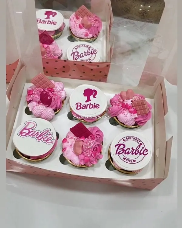 A box of custom Barbie-themed cupcakes, perfect for a birthday girl. Each cupcake is 100% eggless, with some featuring detailed edible prints and others topped with pink frosting, sprinkles, and chocolate pieces for a truly magical look.
