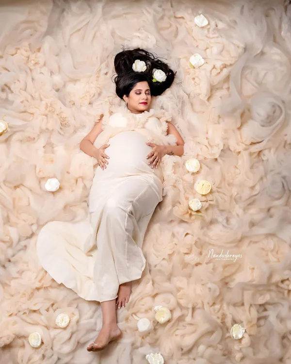 A dreamy and artistic top-down shot, with the mother-to-be lying in a bed of soft, cloud-like fabric and white roses. This is a truly unique and ethereal maternity portrait.