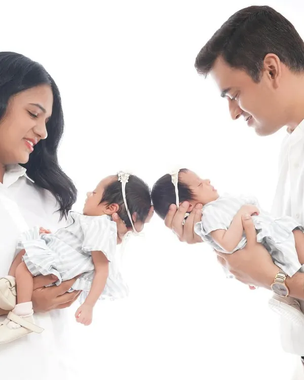 A beautiful, symmetrical portrait of parents holding their newborn twin girls. This pose highlights the joy and wonder of having two new babies to love.
