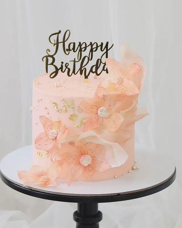 An ethereal and delicate birthday cake. This soft pink cake is adorned with translucent, handcrafted rice paper flowers and touches of gold leaf, creating a light and airy design.