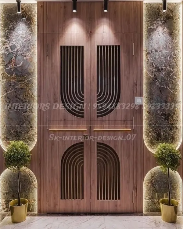 A grand entrance featuring a double door with modern semi-circular grooves. The doors are flanked by marble panels and illuminated niches with planters, creating a luxurious first impression.
