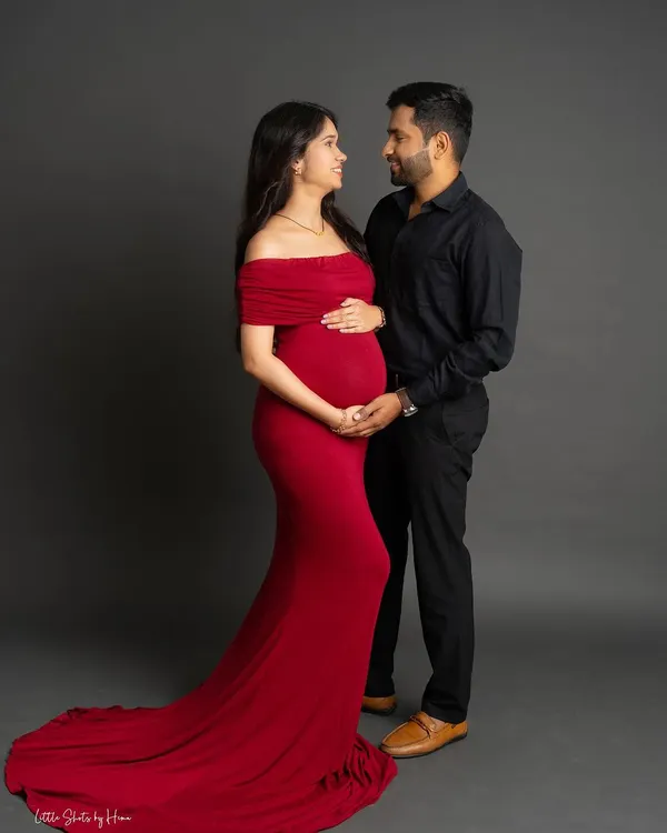 A classic studio portrait for you and your partner. The mom-to-be wears a striking red off-the-shoulder gown, creating a beautiful contrast with her partner's all-black attire as they share a loving gaze.