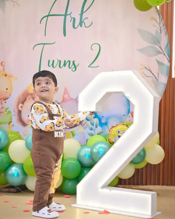 The birthday boy proudly stands next to a giant light-up number '2' at his jungle-themed party.