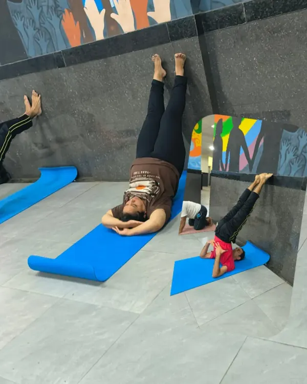 Students in my group class practicing inversions like Sirsasana (headstand) with wall support, ensuring safety for all levels.