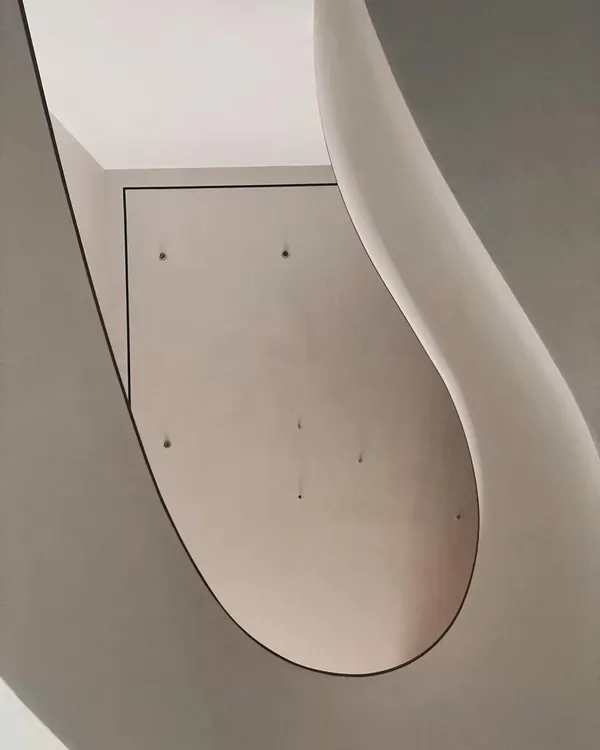 The sweeping curve of the Worli Duplex staircase, viewed from below. The abstract, sculptural quality of the form is revealed by the way it catches and reflects light, creating a fluid, organic shape within the home.
