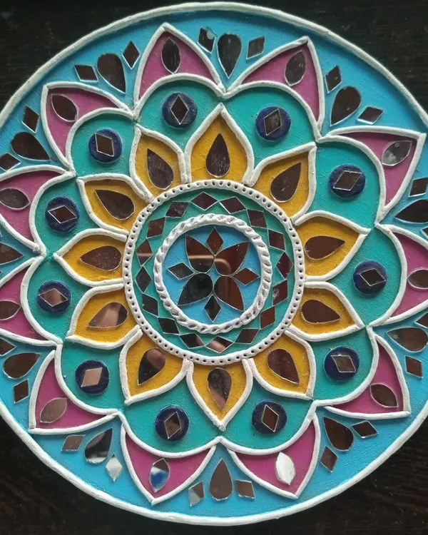 A close-up of a finished Lippan art piece with a floral mandala design. Notice how the combination of bright turquoise, yellow, and pink paint with carefully placed mirrors creates a vibrant, eye-catching effect.