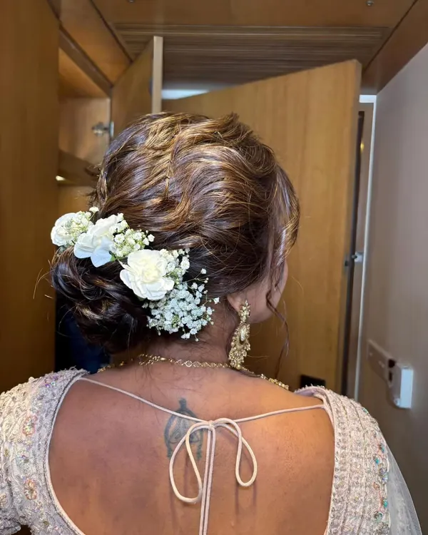 A detailed shot of a beautiful floral bridal bun. The combination of white roses and baby's breath adds a touch of romance and elegance to this classic hairstyle.