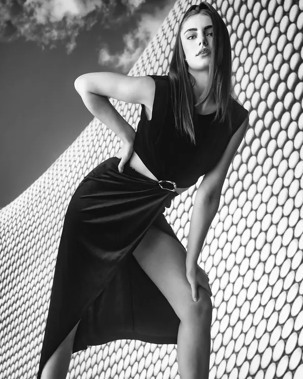 A bold black and white portrait that plays with architectural patterns and strong diagonal lines. The high contrast and the model's powerful pose create a striking and modern composition.