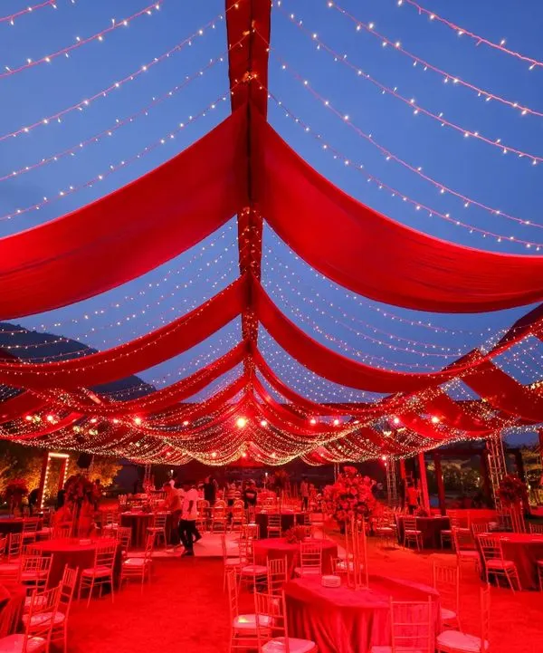 As dusk settled, the reception tent came alive. The vibrant red drapes glowed against the evening sky, creating a dramatic and romantic atmosphere for an unforgettable night of celebration.