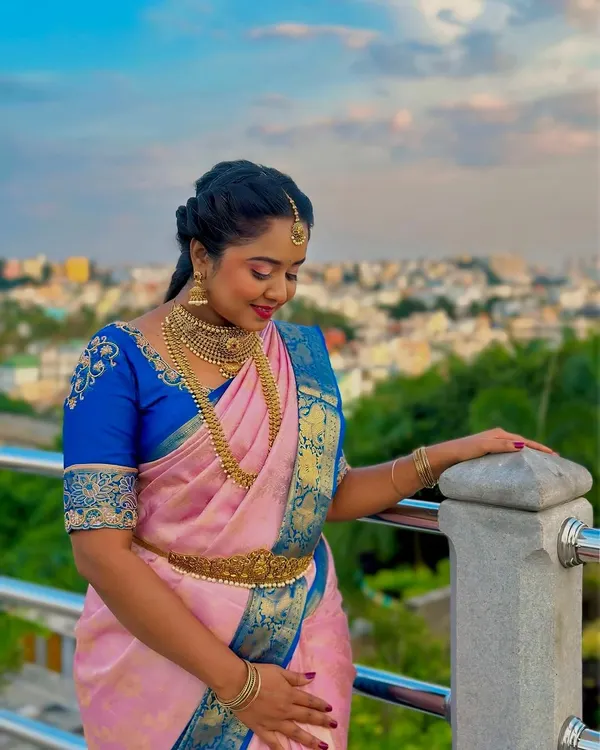 A beautiful model shoot featuring a traditional South Indian look. I paired a pink and blue silk saree with heavy gold jewelry, a braided hairstyle, and makeup featuring a sharp wing and red lips.