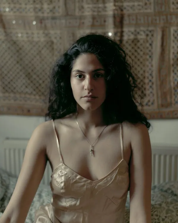 An intimate portrait of Riya Miam in her London home, capturing a quiet and direct gaze in a soft, natural light setting.