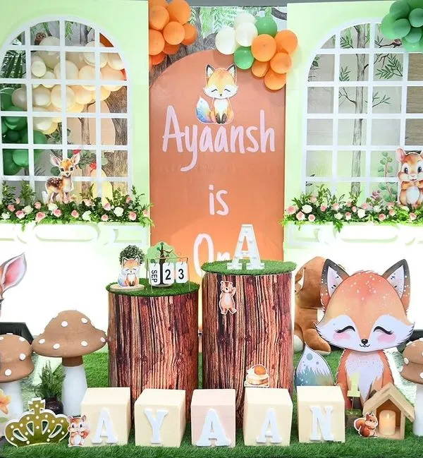 A full view of the woodland jungle theme for Ayaansh's first birthday. This large scale decoration features a custom backdrop, adorable animal figures like a deer and fox, and organic balloon garlands.