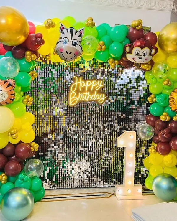 This vibrant Jungle Safari theme is perfect for a first birthday party. The setup features a sparkling shimmer wall, a custom neon sign, a large marquee number '1', and a full organic balloon arch with fun animal-shaped foil balloons.