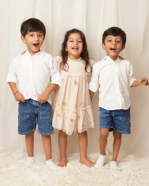Three older siblings stand together, laughing with wide-open mouths. This candid shot captures the pure joy and energy of their relationship.