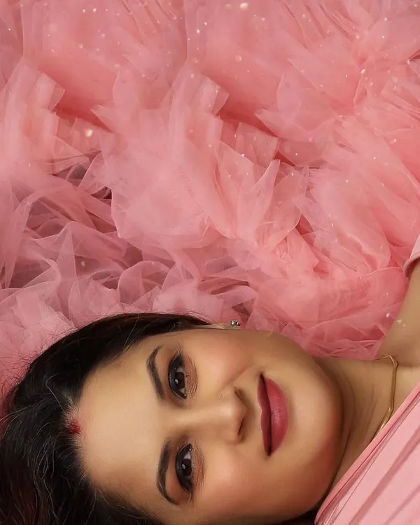 A close-up portrait focusing on the serene expression and flawless makeup of the mom-to-be, surrounded by a cloud of soft pink tulle.