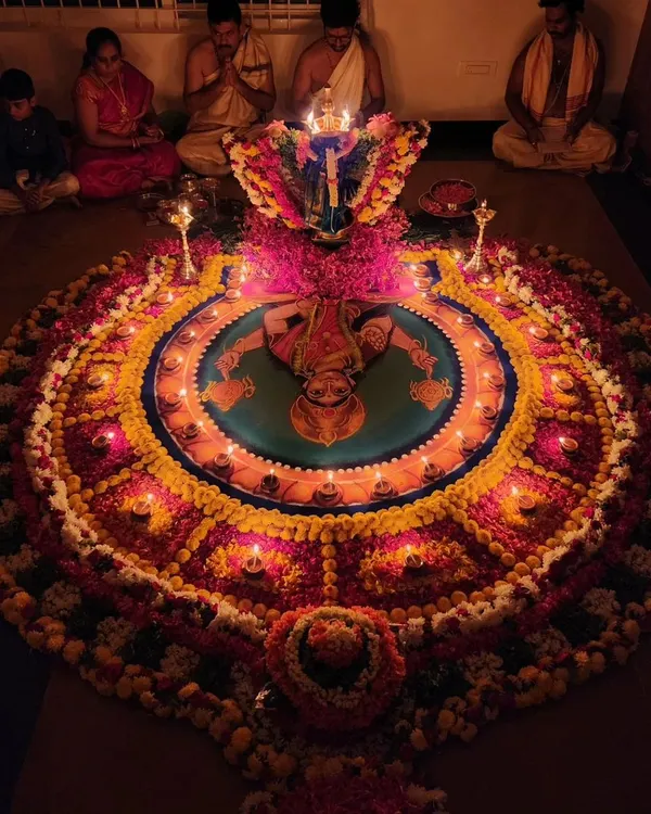 This is a Durga Deepa Namaskara pooja, a powerful ceremony for invoking the Goddess's blessings for health, wealth, and prosperity. The intricate rangoli and the glow of numerous lamps create a spiritually charged atmosphere for the devotees.